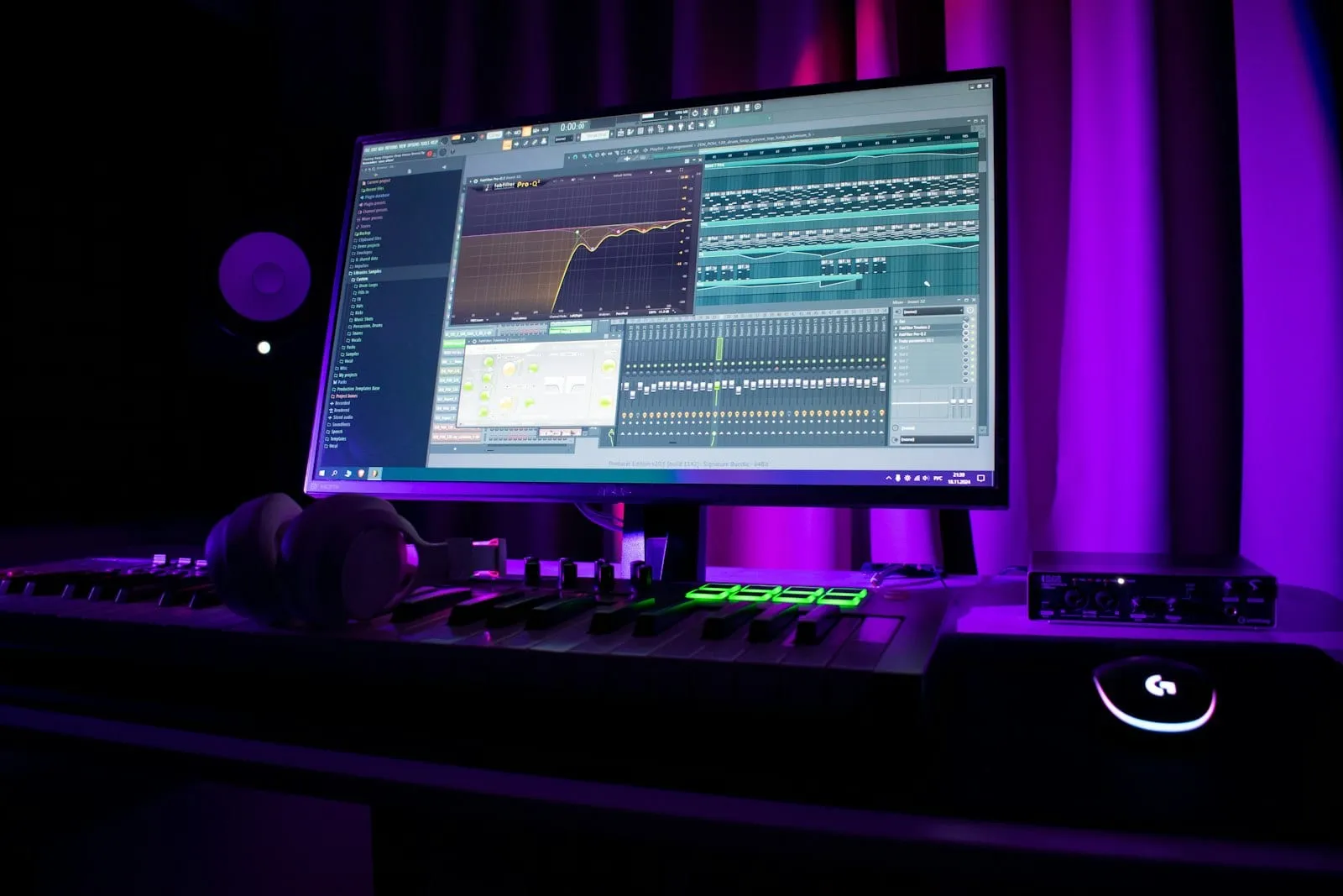 A producer's desk with a loop open in a DAW, MIDI keyboard, and headphones
